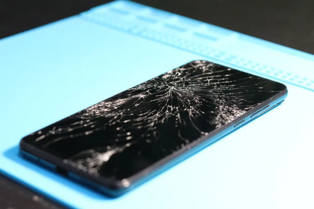Móvil Android con la pantalla rota sobre la alfombrilla de reparación
